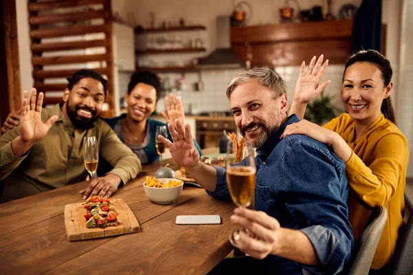Multi-ethnic group of people having fun and waving while drinking wine and looking at camera.