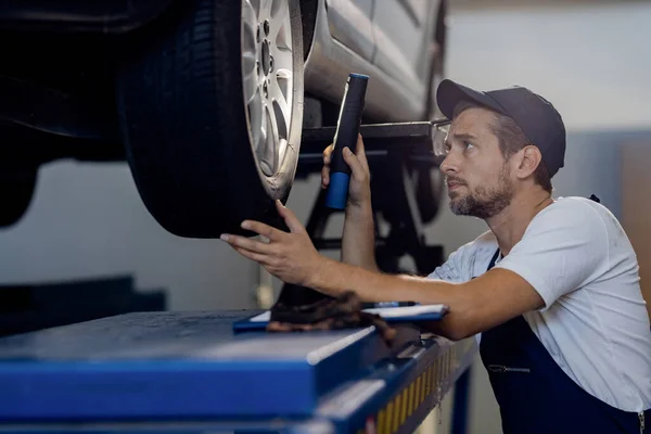 Mid Adult Mechanic Examining Car Tire Flashlight While Working Auto —  Fotos de Stock
