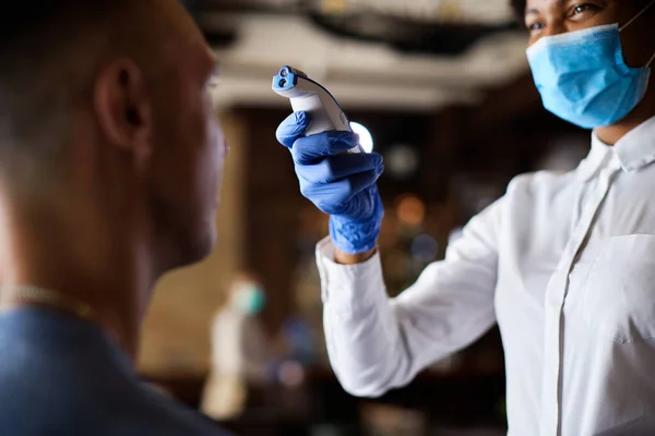 Close-up of waitress using infrared thermometer and measuring customer\'s temperature in a cafe during coronavirus epidemic.