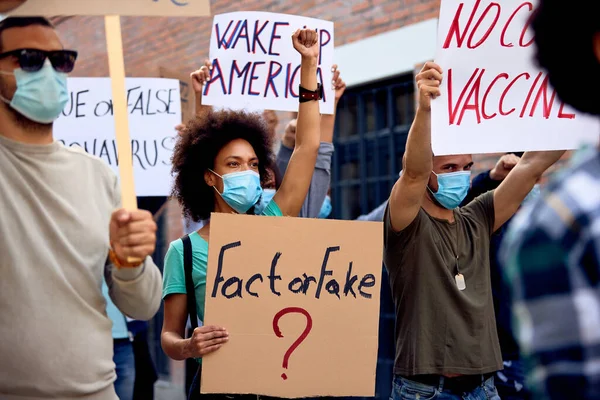 African American woman wearing protective face mask while standing among crowd of people and protesting against coronavirus government measures.