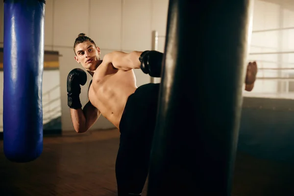 Young dedicated sportsman kicking a bag during sports training at boxing club.