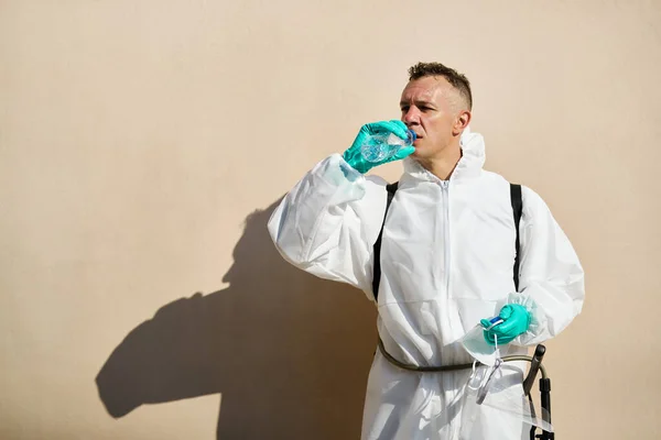 Sanitation worker in hazmat suit having a water break and refreshing himself after disinfecting due to coronavirus pandemic.