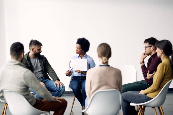 Black female mental health professional examining graph while having a session with group of people. 
