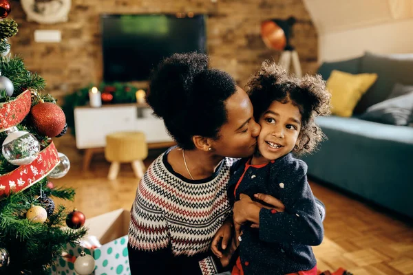 Affectionate black mother kissing her daughter while spending Christmas together at home.
