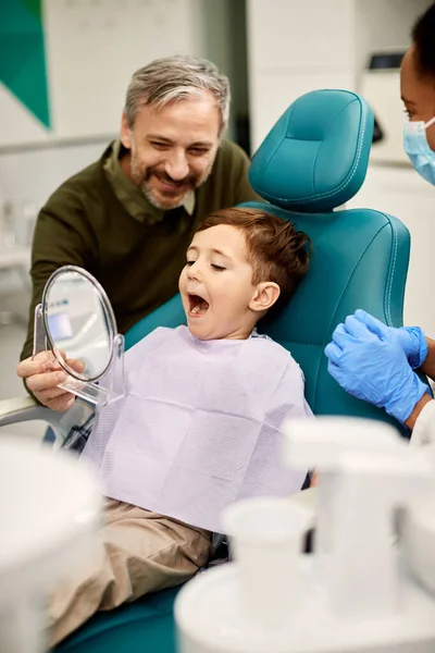 Small boy with mouth open checking his teeth in a mirror during appointment at dentist\'s office.