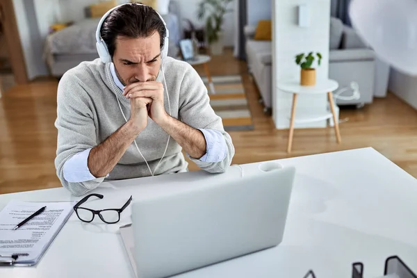 Young worried businessman using computer and reading an e-mail while working at home.