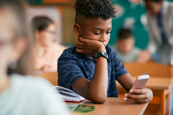 African American schoolboy using smart phone during a class in the classroom.