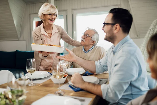 Happy Mature Woman Serving Lunch While Talking Her Family Dining — Foto Stock