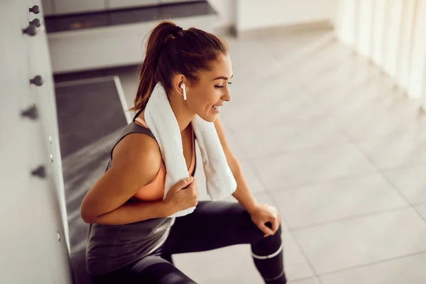 Happy Female Athlete Listening Music Wireless Earphones While Relaxing Locker — Stockfoto