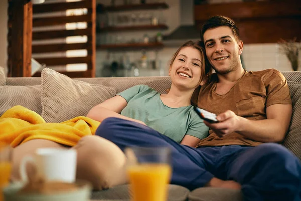 Young happy couple changing channels on TV while relaxing in the living room.