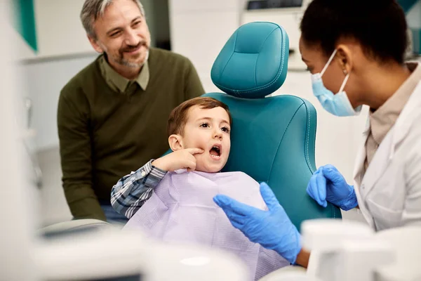 Little boy talking about his toothache with dentist while being with his father at dental clinic.