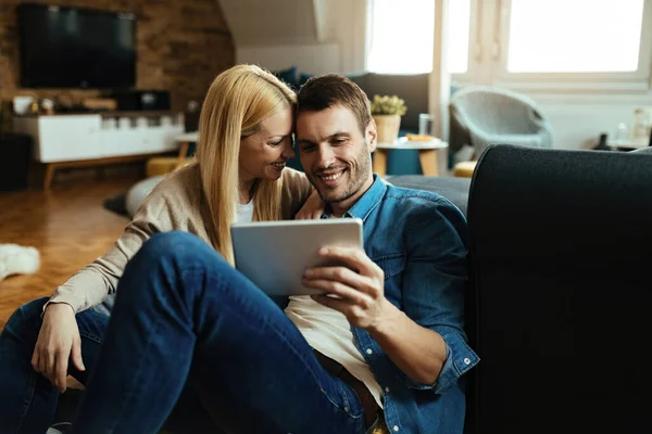 Young happy couple surfing the net on touchpad while relaxing in the living room.