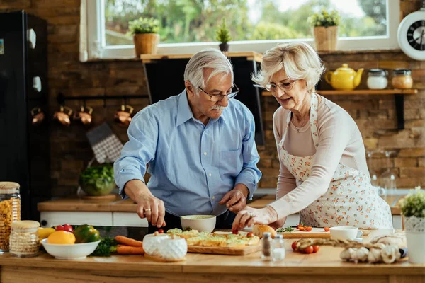 Mature husband and wife cooperating while preparing bruschetta in their kitchen. 