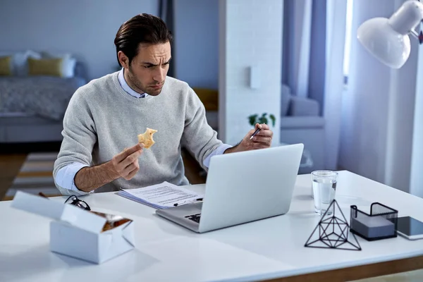 Young Freelance Worker Using Laptop Eating While Working Home — Photo