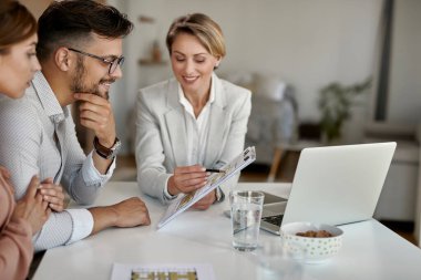 Young couple examining blueprints with their real estate agent while having a meeting in the office. Focus is man.