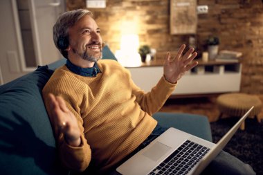 Happy businessman using computer and making conference call while working late at home. 