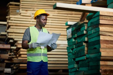 African American warehouse worker analyzing delivery plans at wood storage compartment.