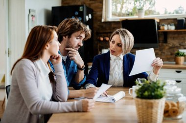 Financial advisor communicating with young couple while going through their financial reports during a meeting at home. 