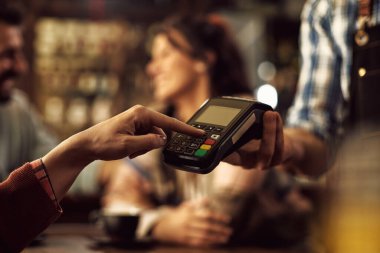 Close-up woman entering pin at credit card reader while paying in a cafe. 
