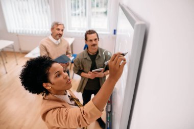 African American professor giving lecture to her adult students and writing on whiteboard during a class. 
