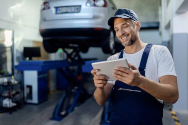 Happy mechanic using digital tablet at auto repair shop.