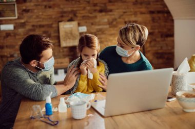 Caring parents wearing protective face masks while their daughter is feeling sick and blowing nose at home. 