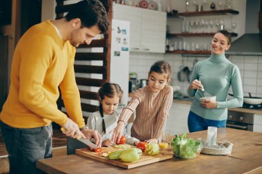 Happy family enjoying while preparing healthy meal and chopping vegetables in the kitchen. 