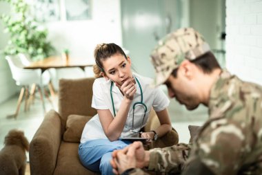 Young female doctor feeling worried while talking to military officer at home. 