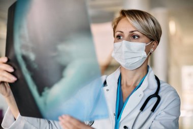 Medical expert wearing face mask while examining X-ray scan at the clinic. 