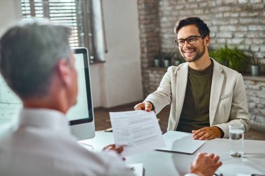 Young happy man applying for job and giving his CV to a manager during the interview in the office. 