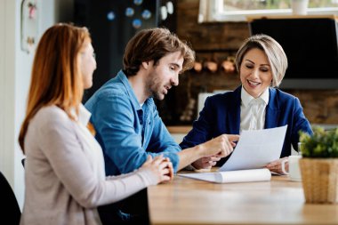 Young couple and insurance agent analyzing documents while having a meeting at their home. Focus is on agent. 