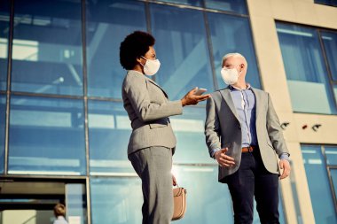 Low angle view of business colleagues with protective face masks communicating while standing in front of office building. 