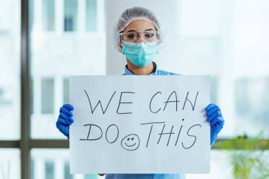 Healthcare worker holding placard with supportive 'we can do this' message while standing in the hospital. 