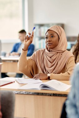 Muslim university student raising her hand to answer a question attending a class in the classroom.