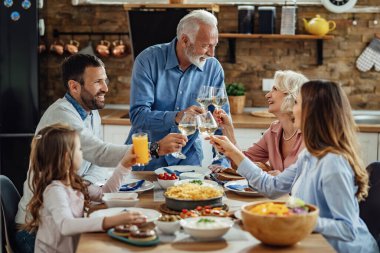 Happy extended family enjoying in a lunch and toasting at dining table. Focus is on senior couple. 