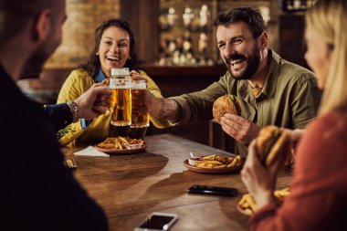 Cheerful man and his friends toasting with beer while eating hamburgers in a pub.