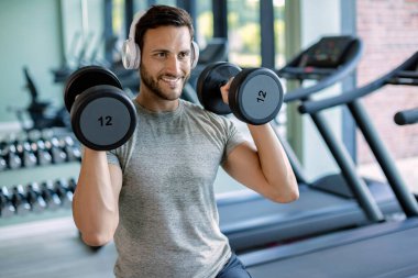 Happy athlete exercising with hand weights during cross training in a gym. 