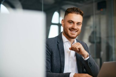 Happy male entrepreneur working on a computer at corporate office and looking at camera.