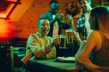Happy African American woman and her friends having fun and toasting with beer  while gathering in a bar.