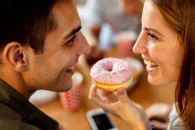 Close-up of happy couple looking at each other while eating glazed donut. 