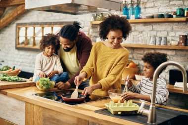 Happy black parents and their kids preparing food in the kitchen. Focus is on mother. 
