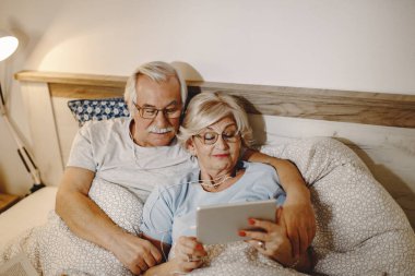 High angle view of senior couple using touchpad while resting in bedroom. 