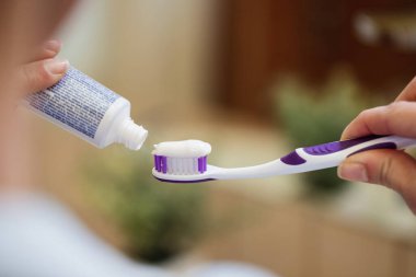 Close-up of unrecognizable woman applying toothpaste on toothbrush in the bathroom. 