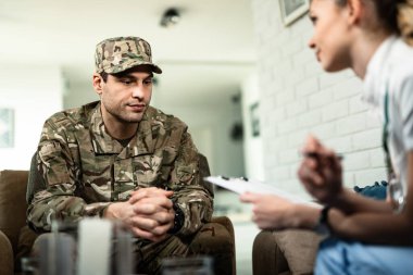 Young distraught soldier talking to female doctor at home. 