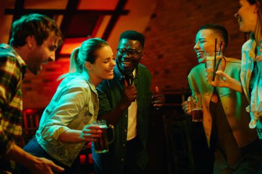 Young cheerful friends singing karaoke and having fun while gathering on night party in a pub. 