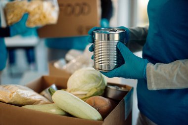 Close-up of unrecognizable volunteer packing donated food in cardboard box and charitable foundation. 