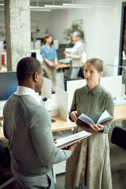 Two business colleagues talking while working at corporate office. Focus is on businesswoman. 