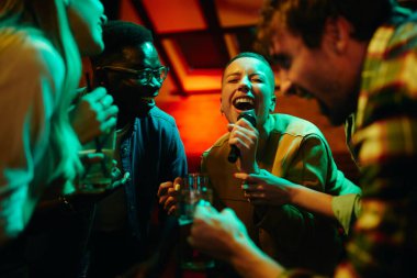 Group of carefree friends singing karaoke and having fun on night party in a bar. Focus is on black woman singing.