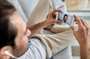 Close-up of man relaxing at home and having video call with hi girlfriend over mobile phone. 