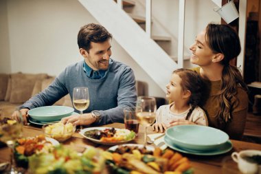 Happy parents with daughter enjoying in conversation during a meal at dining table.